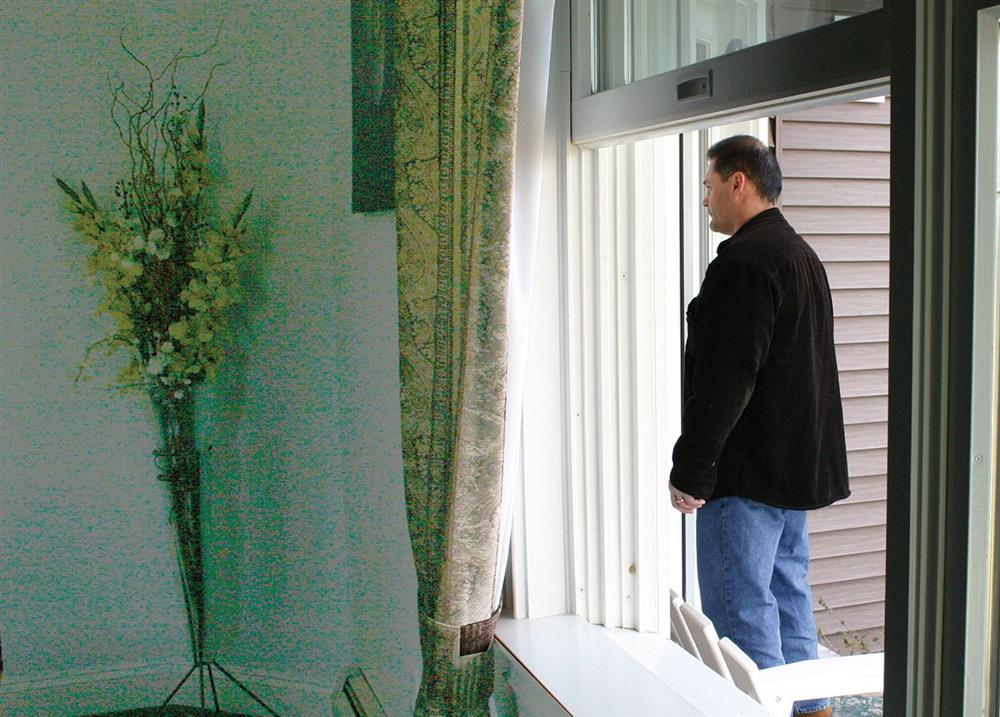 view of a man standing at the front door of a house from a bedroom window