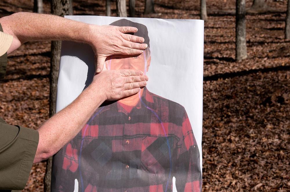Man holding his hands over a paper target to show the cranial vault region of the head for a defensive shooting