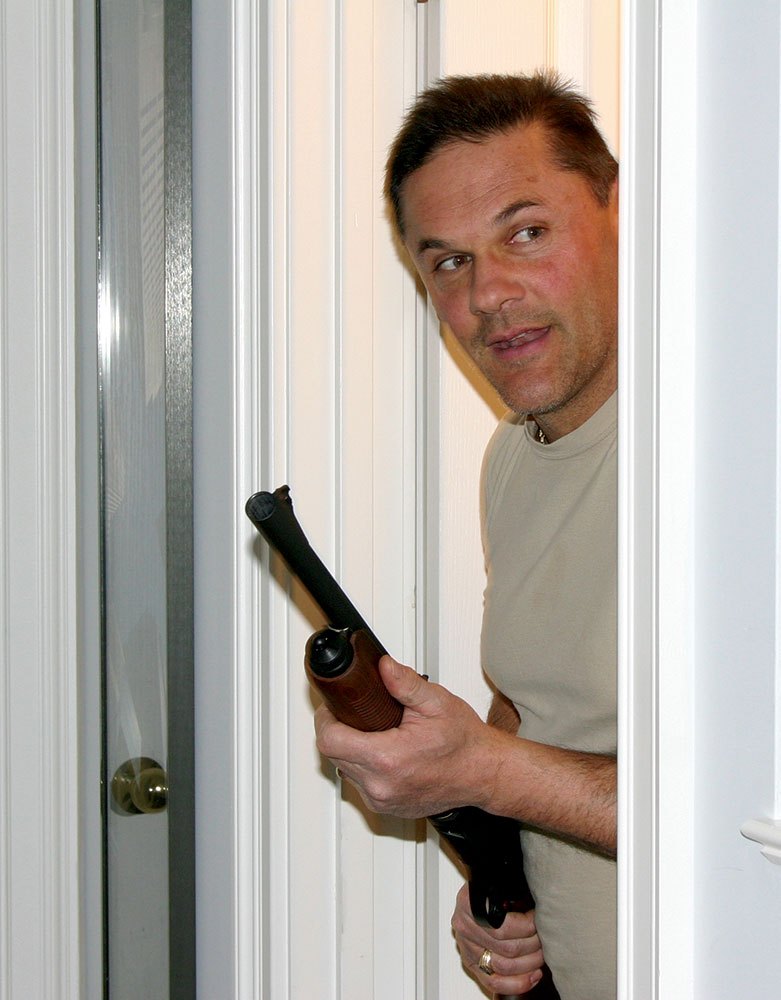 Man peeking through a doorway holding a shotgun