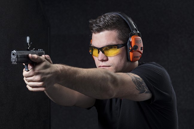 Man with orange earmuuf shooting a pistol with a two-handed grip