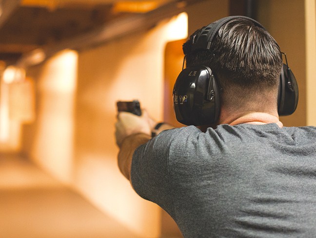 Rearview of man shooting a pistol at an indoor range