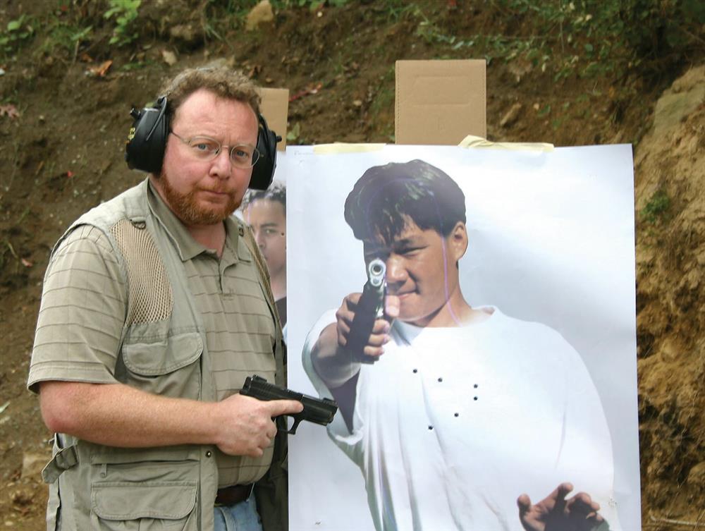 David Kenik holding a pistol showing a fist-sized group on a photo target