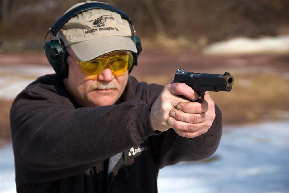 Man wearing safety glasses and hearing protection shooting a 1911 pistol with a two handed grip