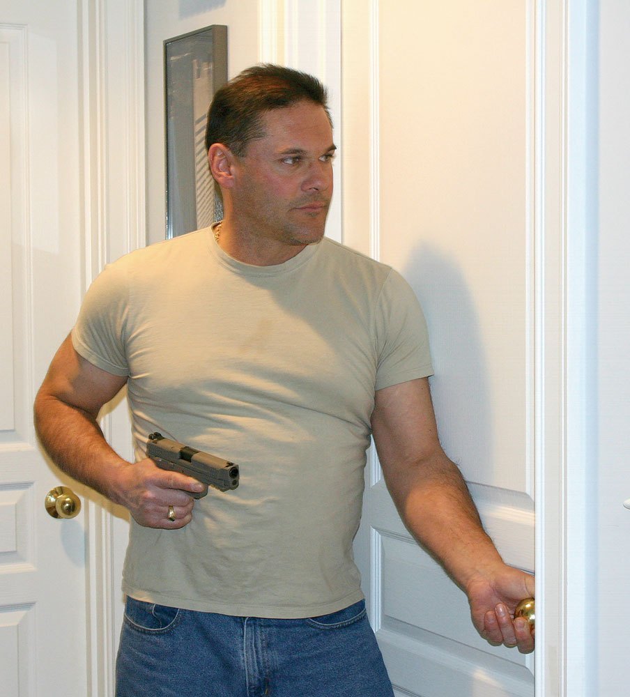 Man holding a pistol while opening a door.